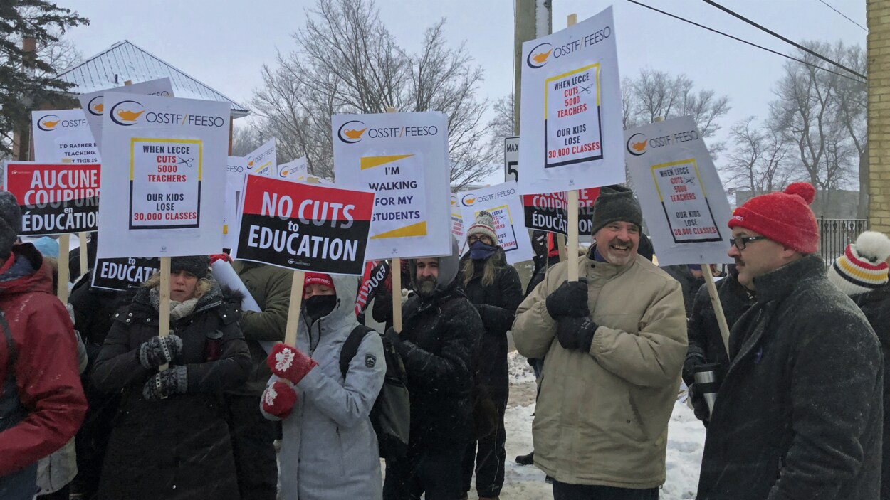 Des syndiqués tiennent des affiches dénonçant les coupes en éducation.