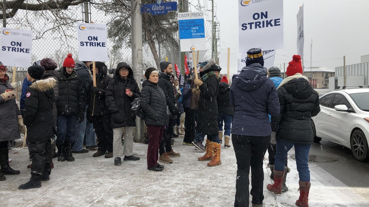 Des manifestants sur le coin d'une rue d'Ottawa avec des pancartes en hiver.