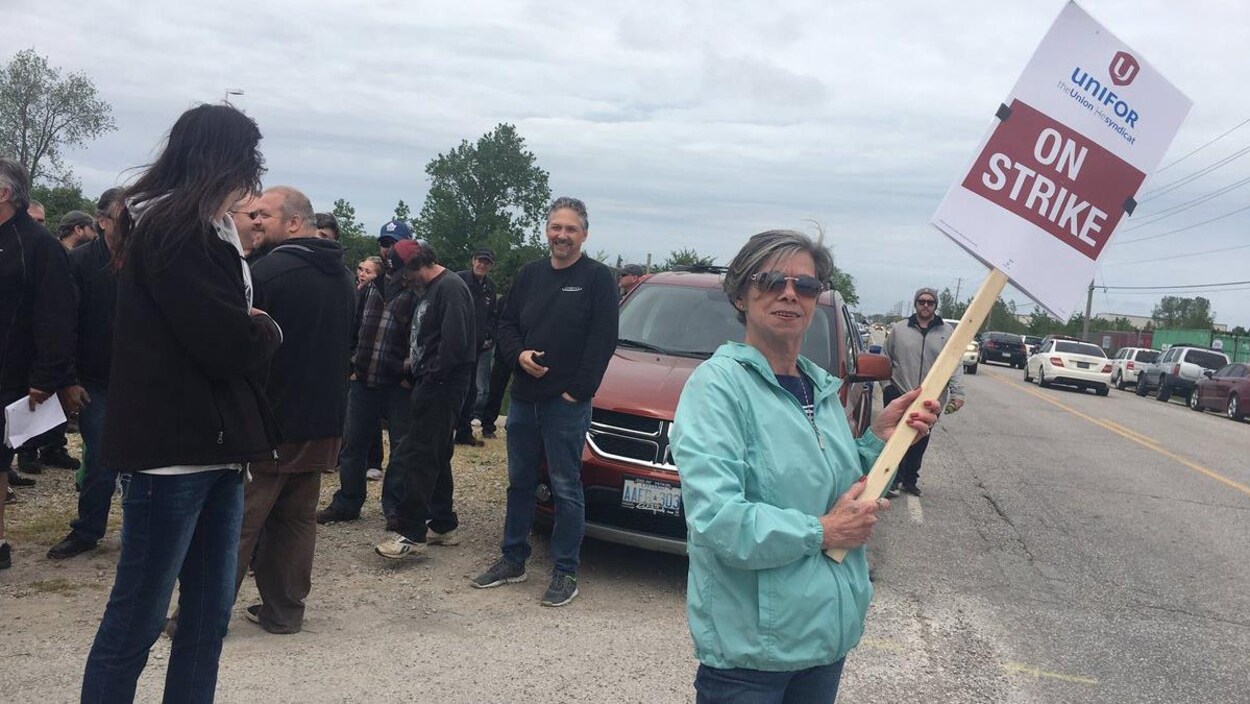 Une femme tient un panneau qui dit "On strike", une foule est en arrière d'elle. Une femme tient un panneau qui dit "On strike", une foule est en arrière d'elle.