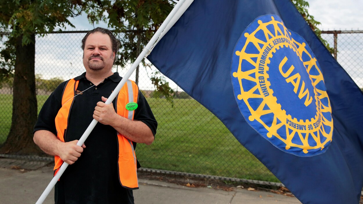 Un travailleur tient dans ses mains un grand drapeau du syndicat United Auto Workers