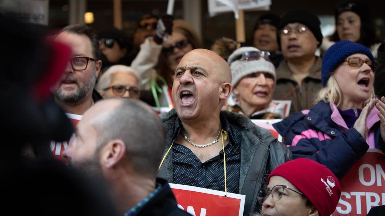 Des personnes sont rassemblées, certaines avec des pancartes, elles crient.