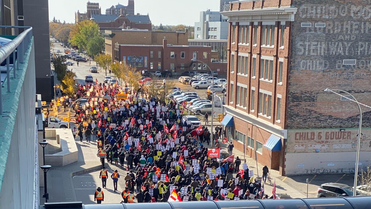 Vue aérienne des manifestants qui défilent dans une rue de Regina. Ils ont des pancartes ou des drapeaux d'Unifor en main.