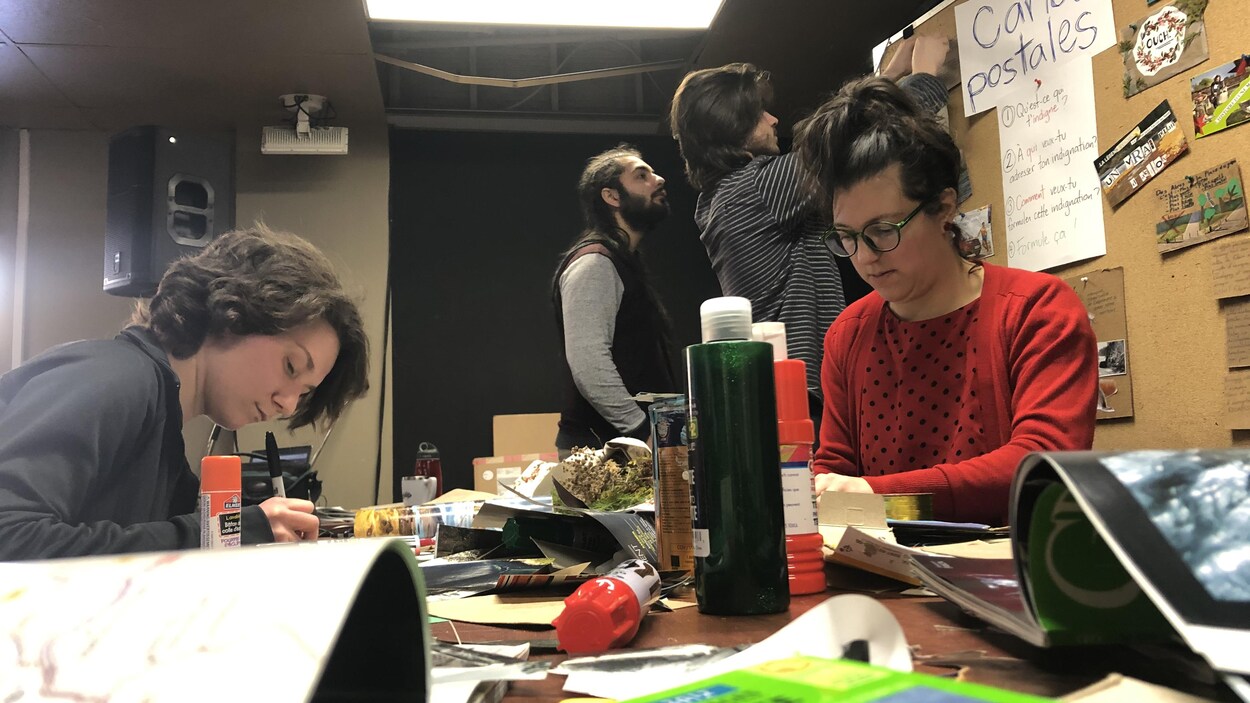 Quatre étudiants bricolent des cartes postales sur un bureau en désordre.