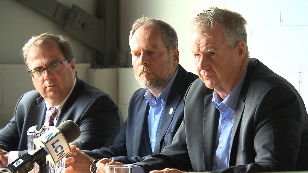 Les trois hommes assis à une table derrière un micro, lors de la conférence de presse.