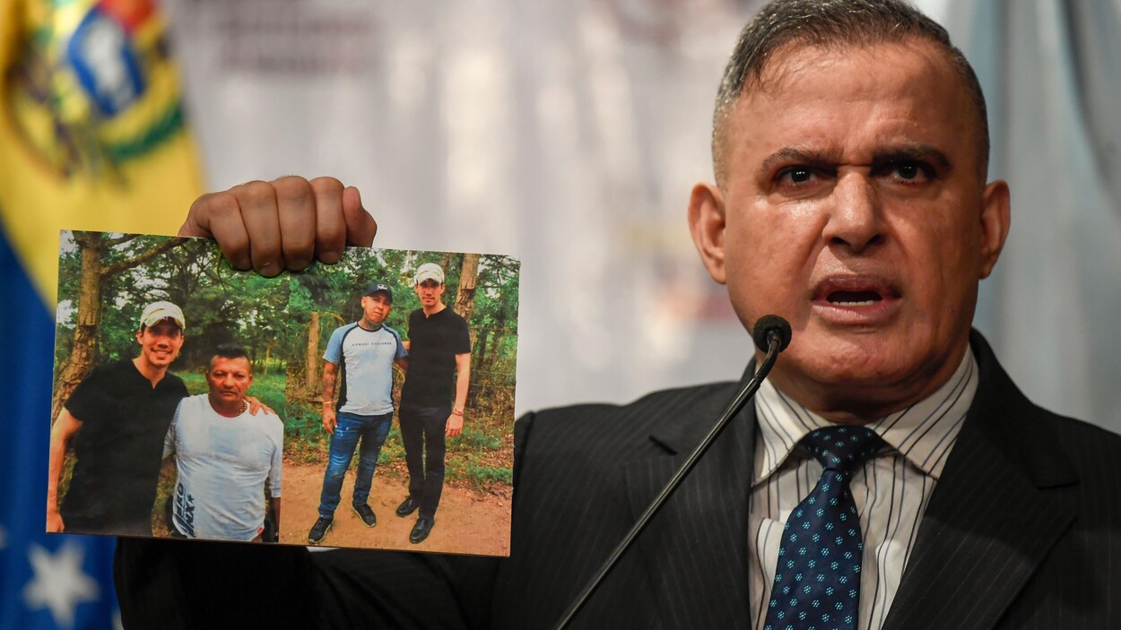 Un homme tient en main deux photos sur lesquelles on peut voir Juan Guaido accompagné de deux autres hommes.