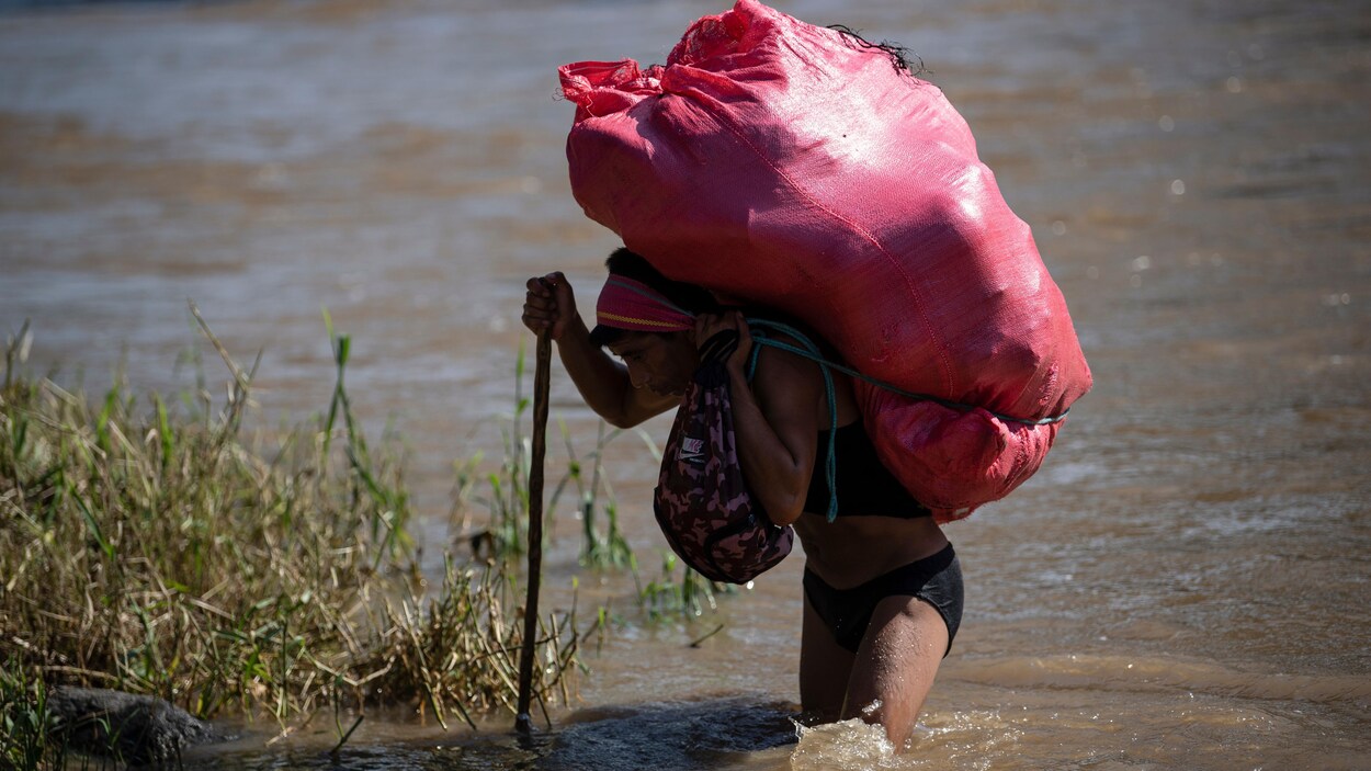 Un homme portant un énorme sac marche dans l'eau en utilisant une canne.