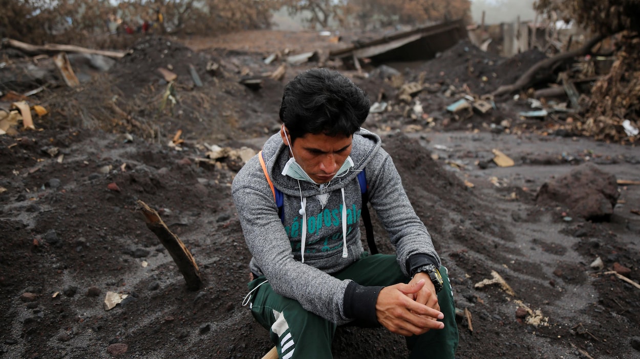 Un homme qui fouille les décombres après l'éruption du volcan de Fuego prend une pause. Le sol est ravagé et les bâtisses en arrière-plan sont démolies. Un homme qui fouille les décombres après l'éruption du volcan de Fuego prend une pause. Le sol est ravagé et les bâtisses en arrière-plan sont démolies.