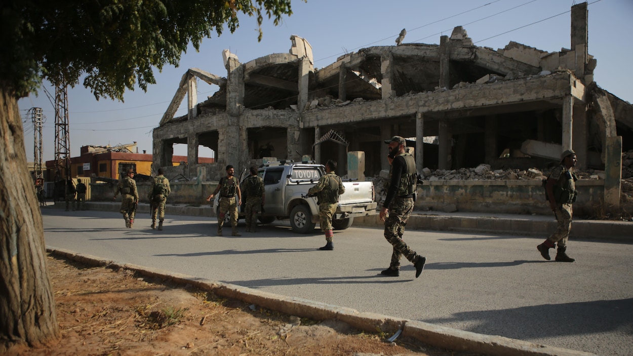 Des combattants patrouillent devant un édifice en ruine.