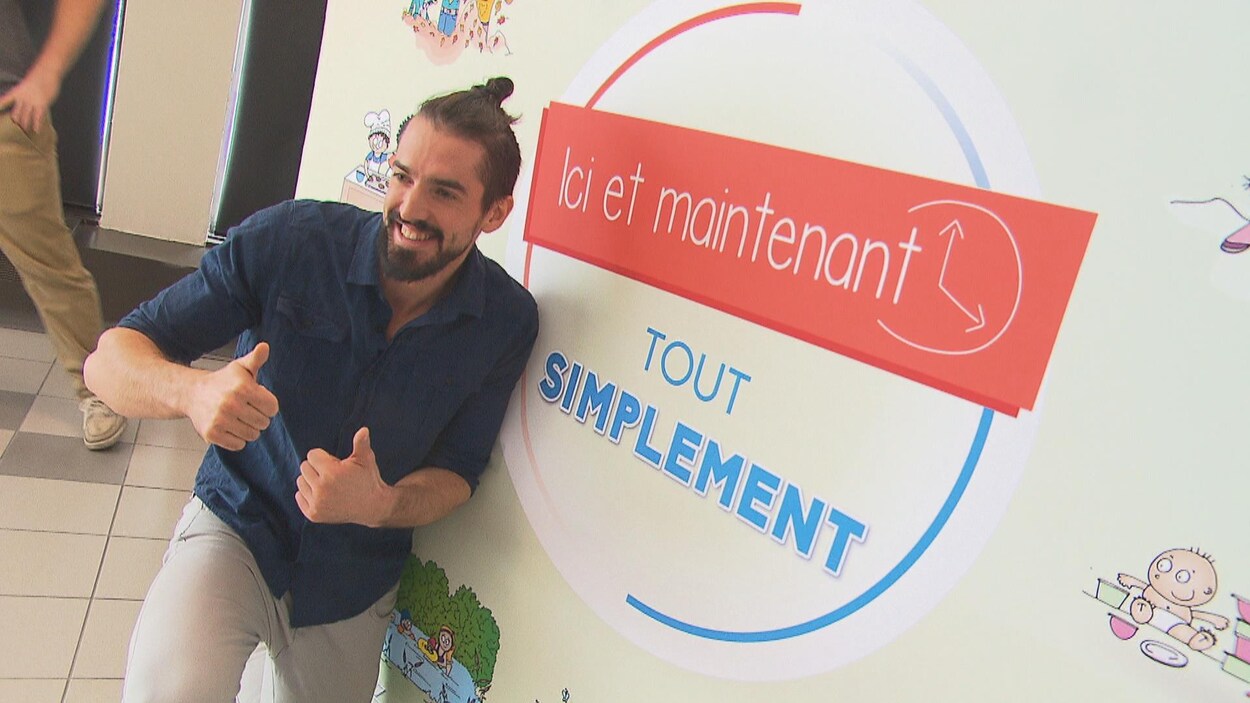 Guillaume Vermette devant une affiche qui dit : Ici et maintenant, tout simplement