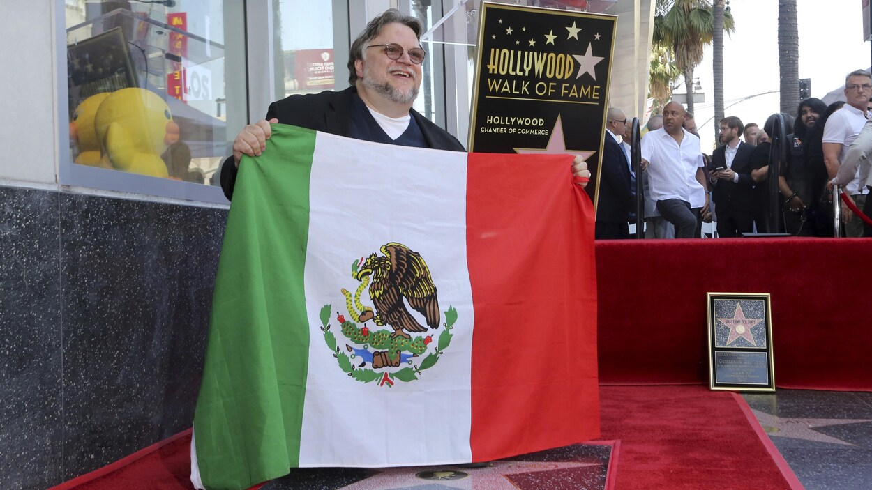 Guillermo del Toro agenouillé près de son étoile et tenant un drapeau mexicain dans ses mains.