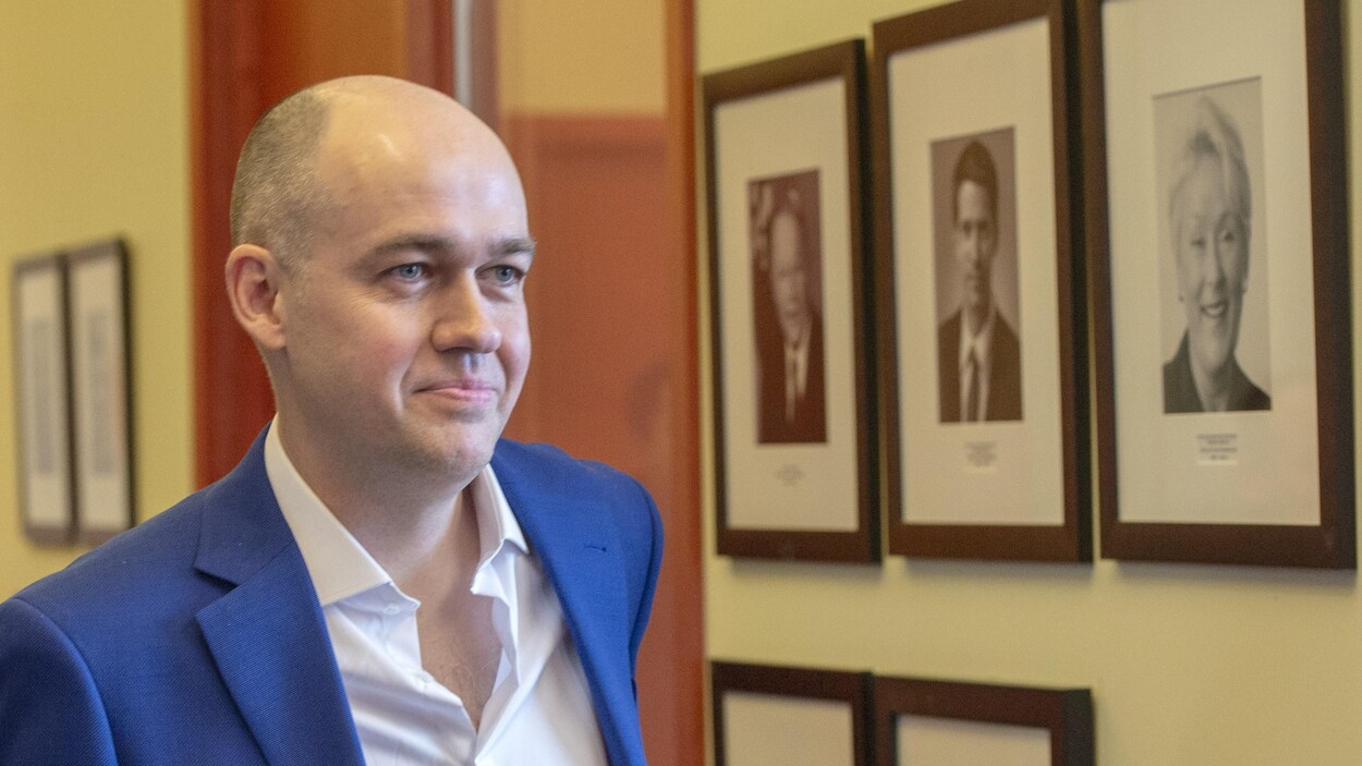 Guy Nantel passe devant des photos de leaders péquistes.