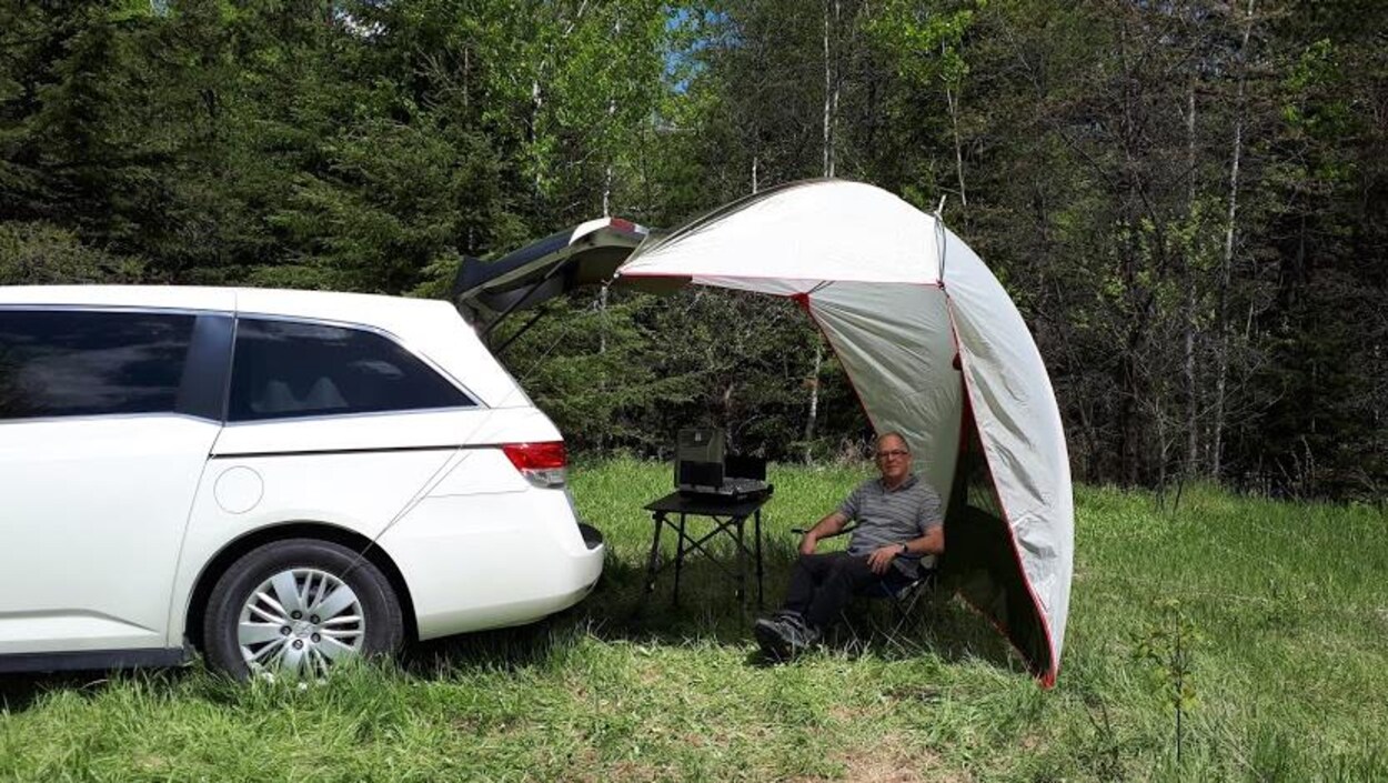 Un homme sous une toile de tente près d'une fourgonnette.