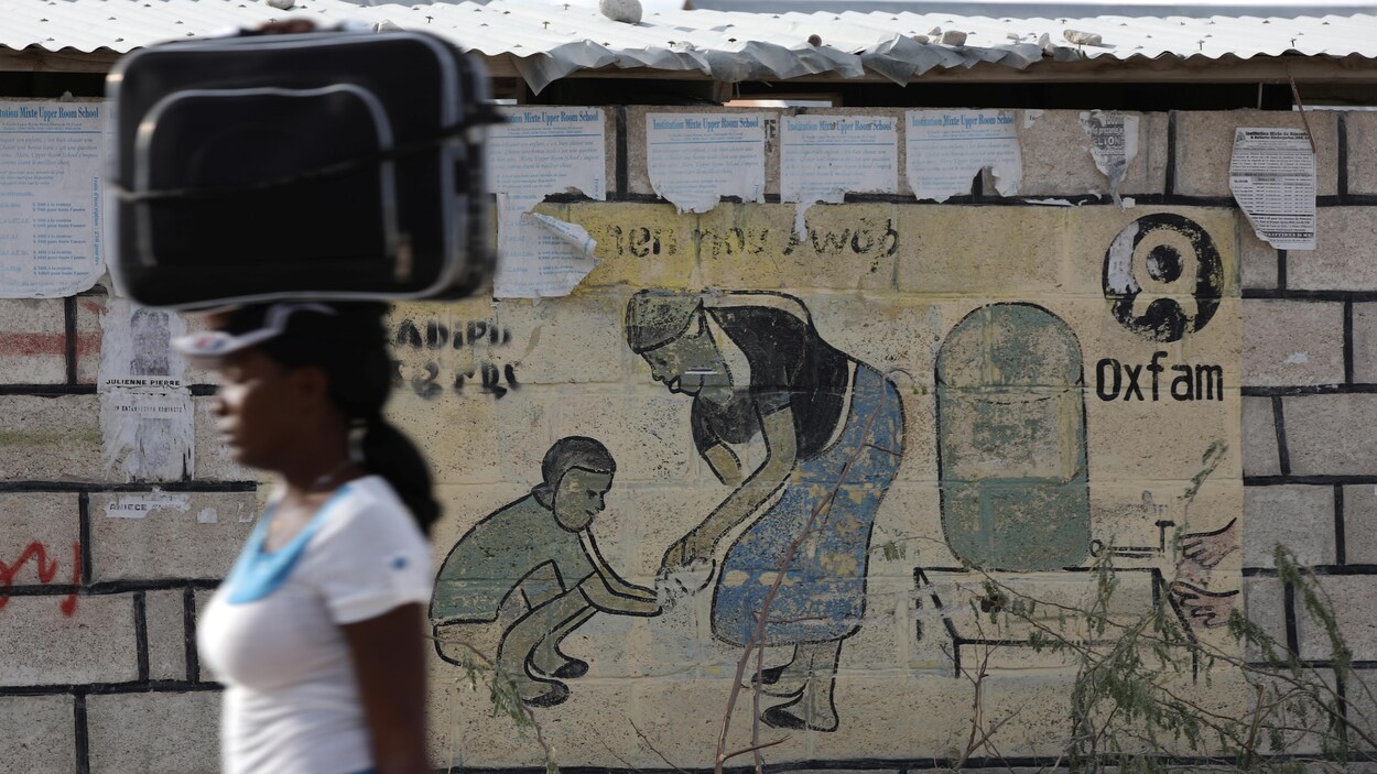 Une femme passe devant une publicité d'Oxfam en transportant une valise sur sa tête. Une femme passe devant une publicité d'Oxfam en transportant une valise sur sa tête.