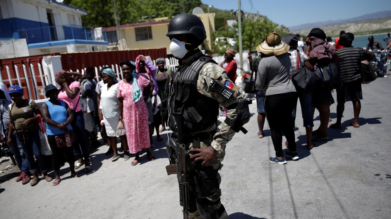 Un agent de police surveille une file tout en portant un masque.