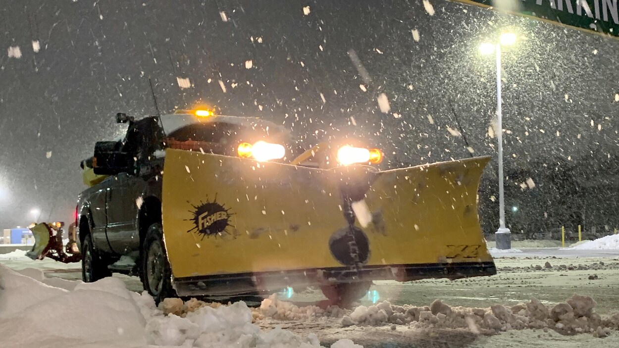 Deux camionnettes munies d'une lame déblaient la neige sur un terrain de stationnement.