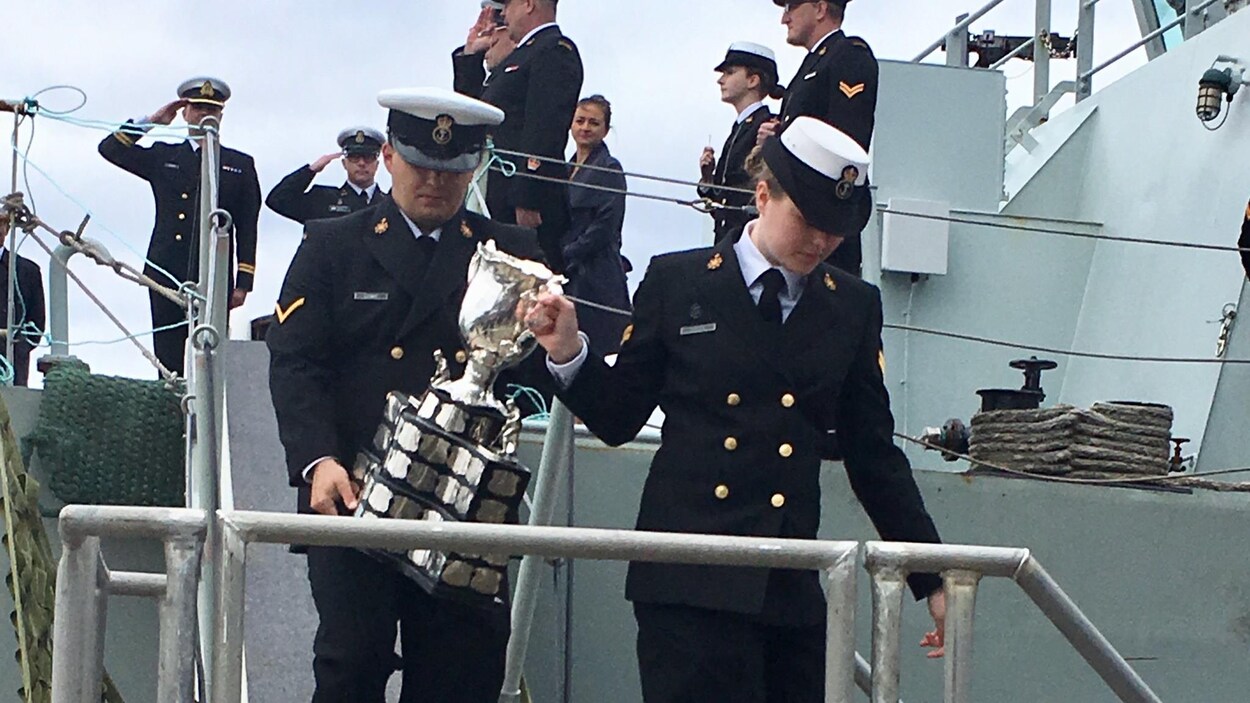 Deux officiers descendent une passerelle en portant le trophée.