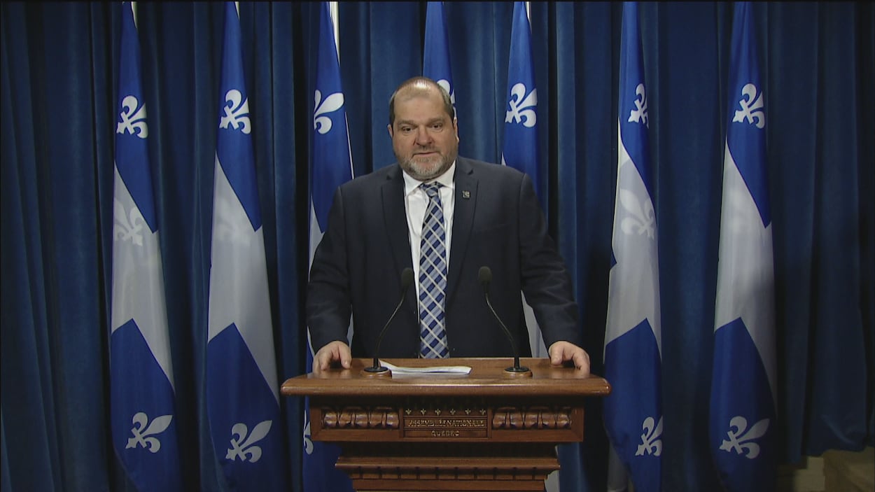 Le député de Rimouski, Harold LeBel au micro, devant plusieurs drapeaux du Québec.