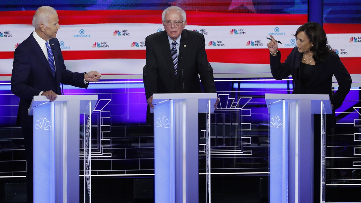 Kamala Harris regarde Joe Biden, la main levée, alors que Bernie Sanders est au milieu des deux candidats.