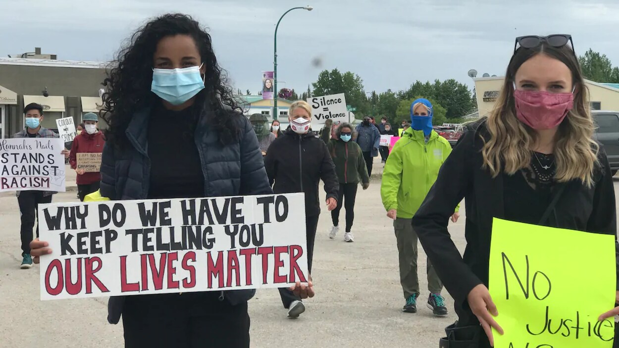 Deux manifestantes portant des masques chirurgicaux tiennent dans leurs mains des pancartes dénonçant le racisme.
