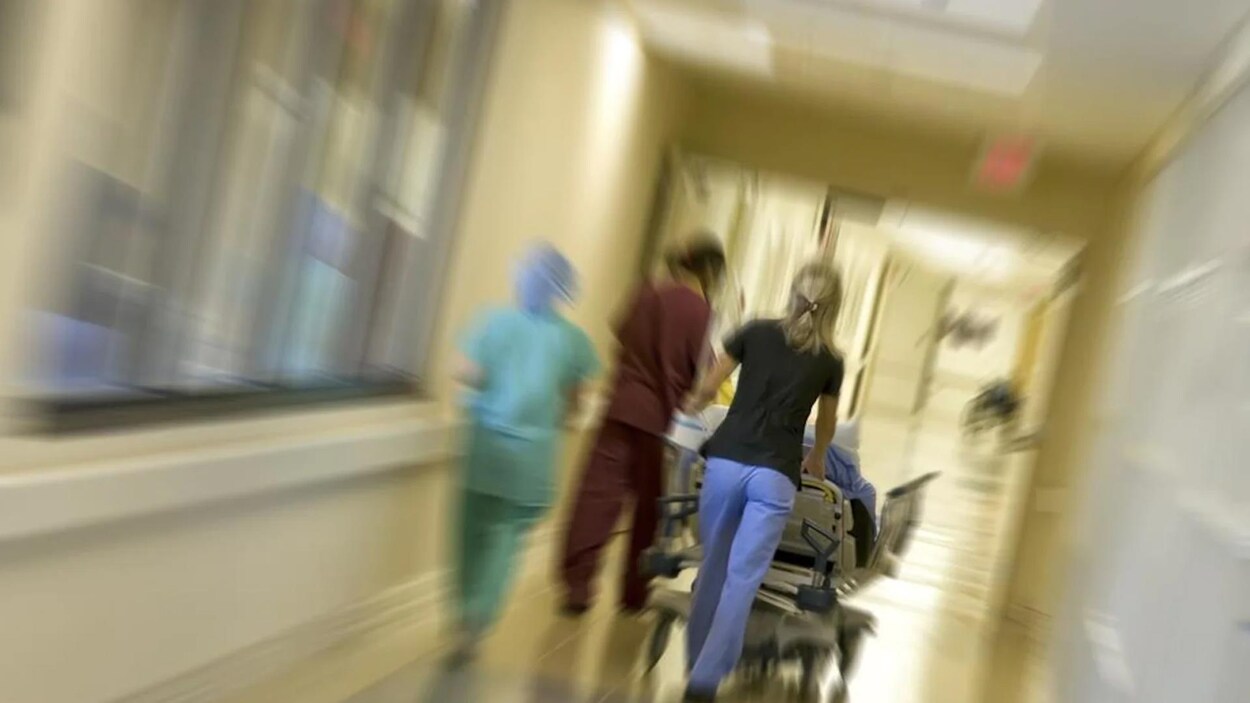 Une infirmière de dos poussant une civière dans un corridor.