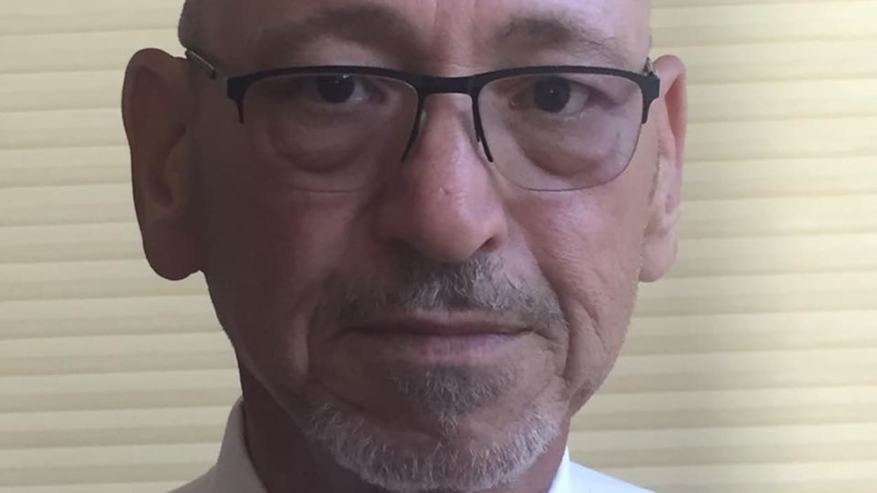 Un homme avec des lunettes devant un store.
