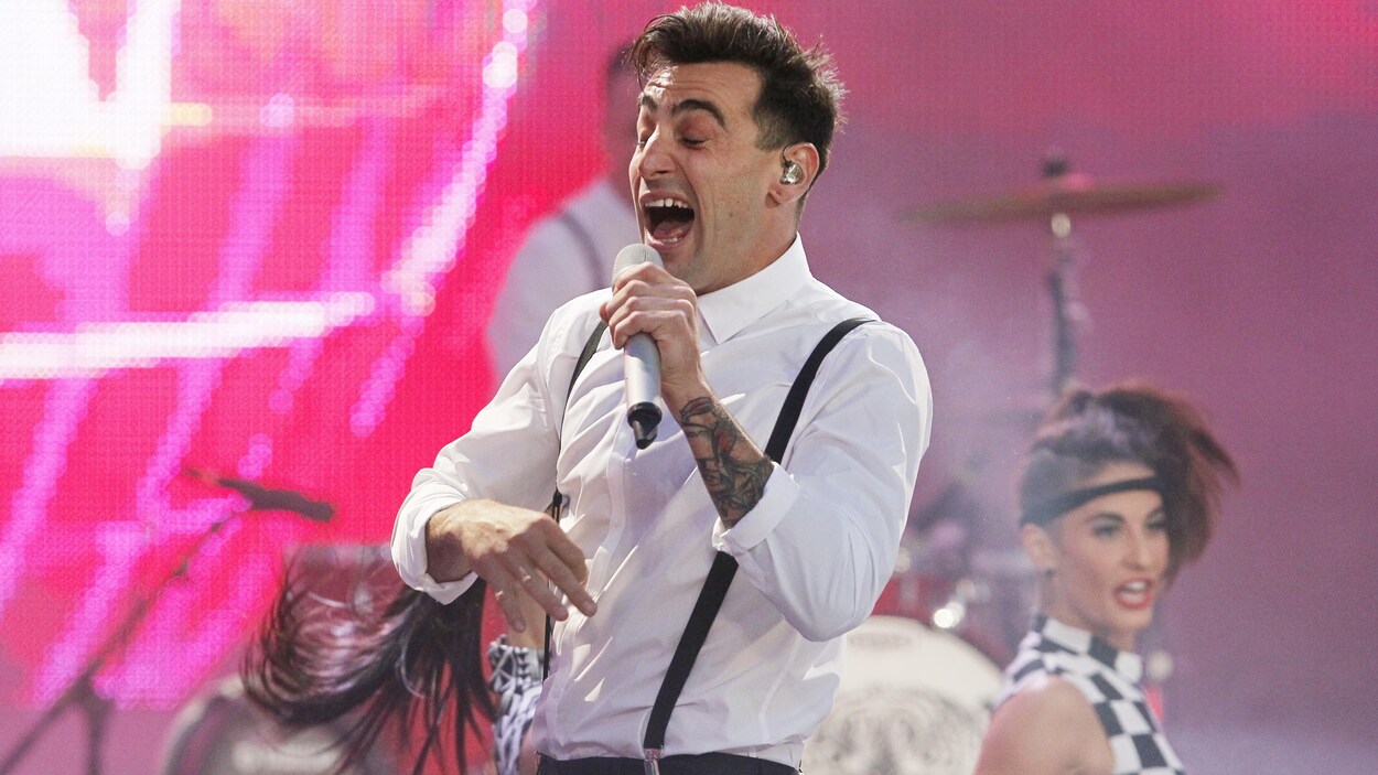 Jacob Hoggard sur une scène. Il tient un micro et on le voit qui chante. Jacob Hoggard sur une scène. Il tient un micro et on le voit qui chante.