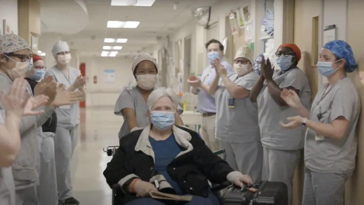 Helen Keene dans un fauteuil roulant sort de l'hôpital sous les applaudissements de travailleurs de la santé.