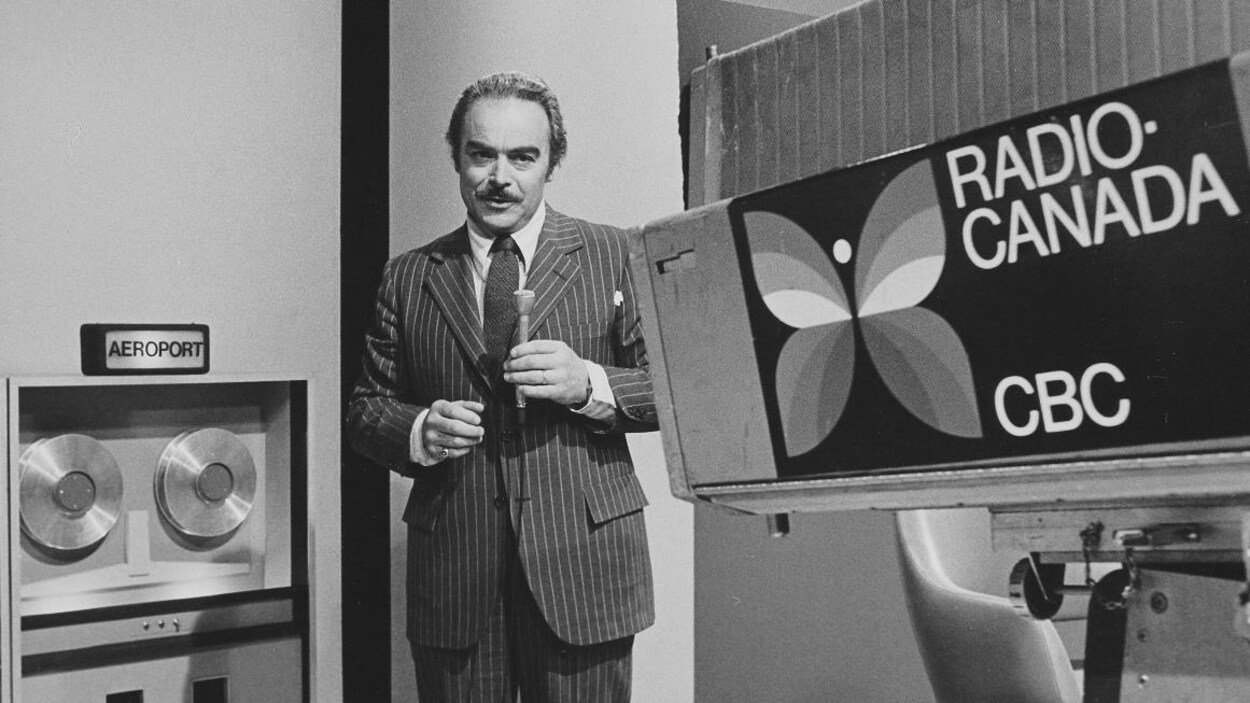 Henri Bergeron animant devant une caméra décoré du logo de papillon de CBC-Radio-Canada.