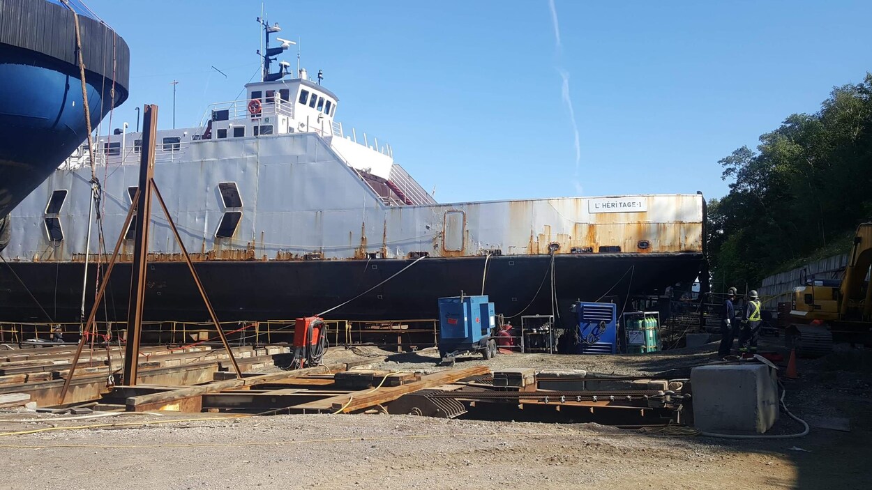 Un navire stationné dans un chantier, entouré d'équipement.
