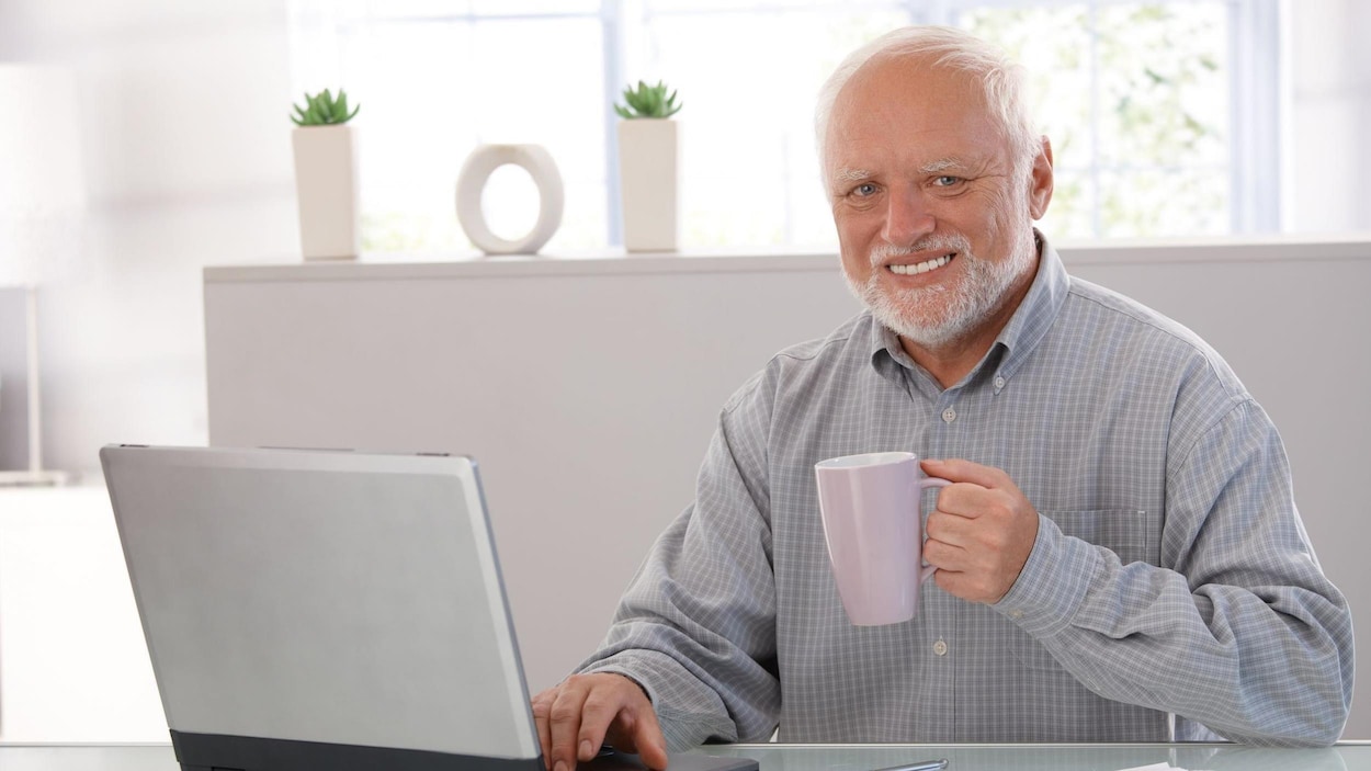 Un homme assis à un bureau tenant un café sourit.