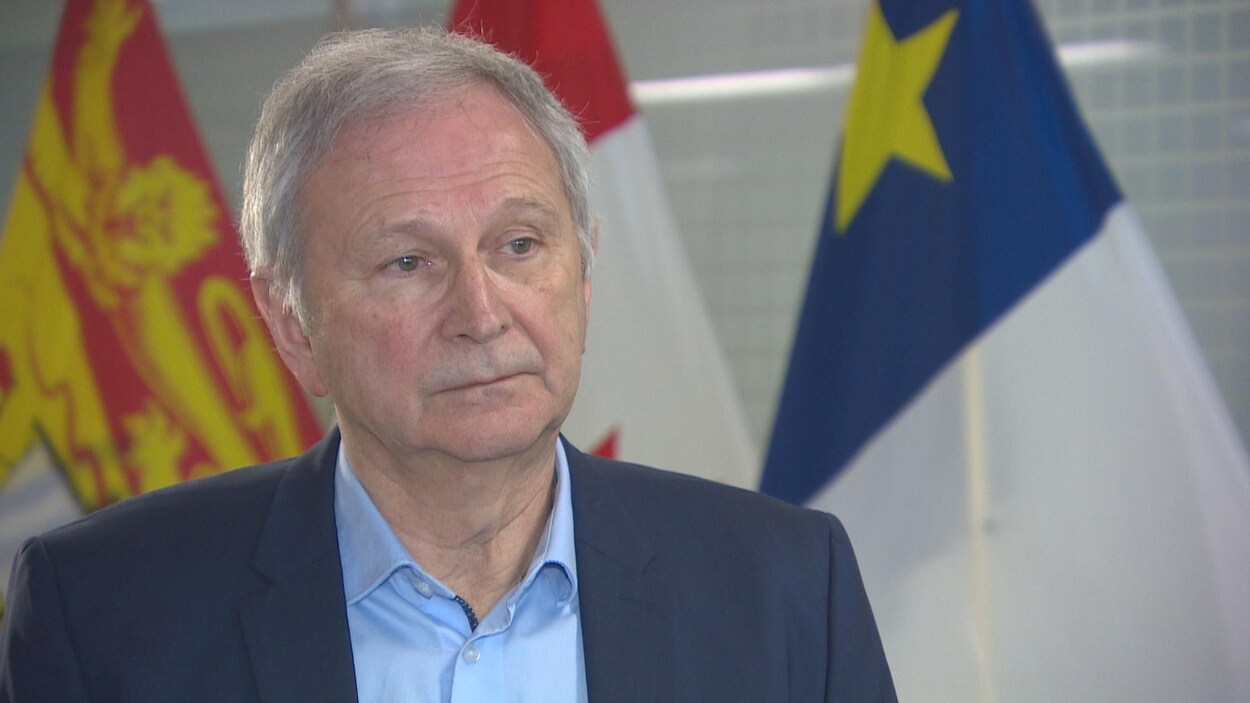 Blaine Higgs en entrevue devant les drapeaux du Nouveau-Brunswick, du Canada et de l'Acadie.