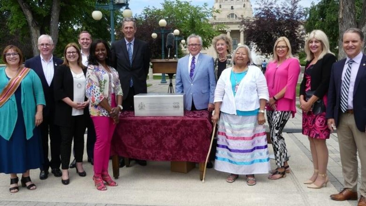 Le premier ministre ainsi que quelques membres du gouvernement et des leaders communautaires debout devant le palais législatif du Manitoba.