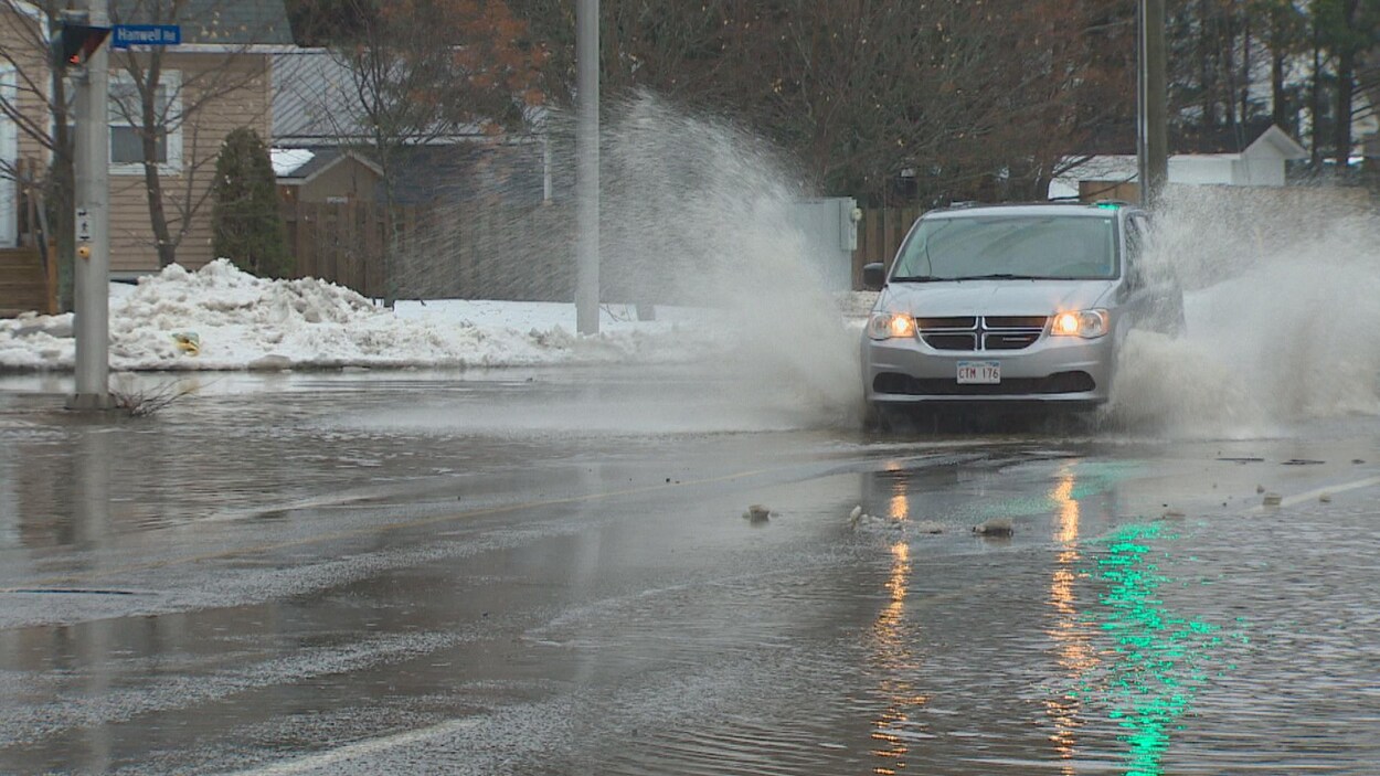 Une voiture circule dans une rue partiellement recouverte d'eau.