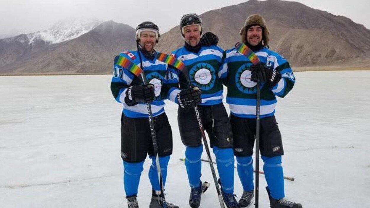 Trois membres de l'équipe The Hockey Foundation prennent la pose sur la glace devant des montagnes de l'Inde. Trois membres de l'équipe The Hockey Foundation prennent la pose sur la glace devant des montagnes de l'Inde.