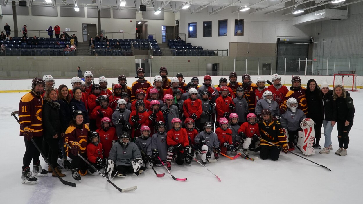 De jeunes joueuses de hockey et leurs mentors prennent une photo de groupe sur la patinoire.