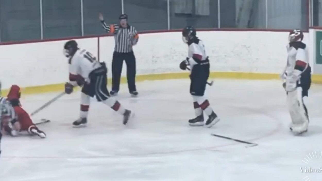 Un joueur de hockey en frappe un autre avec son bâton, un arbitre levant le bras en arrière-plan.