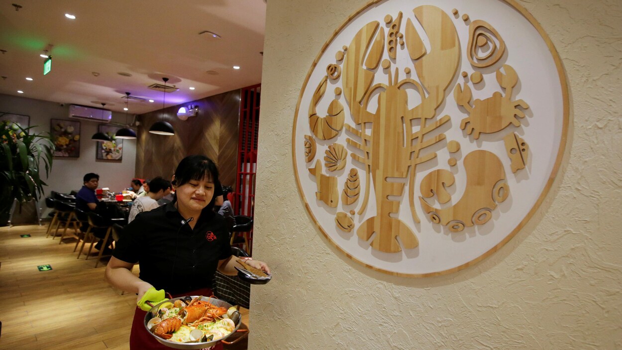 Une serveuse d'un restaurant de Beijing amène un plat de homard vers une table.