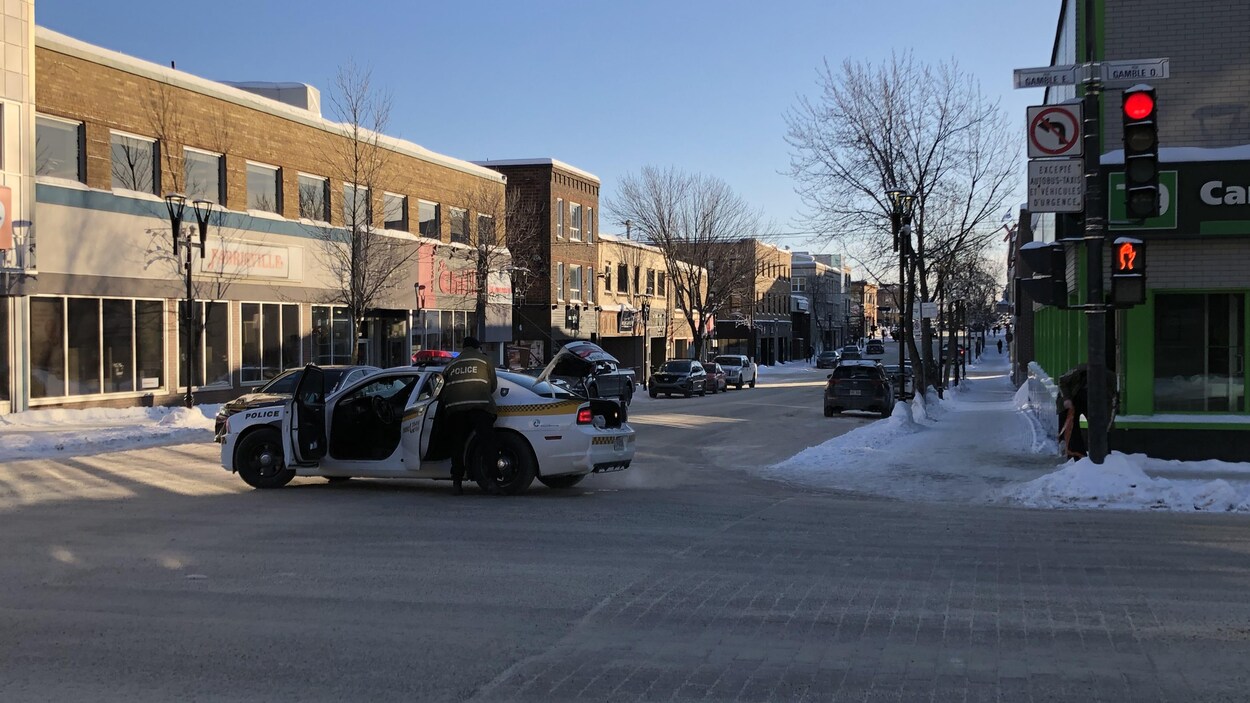 Un policier ouvre une porte d'une voiture de la Sûrté du québec, stationnée au milieu de l'intersection de la rue Gamble et l'avenue Principale.