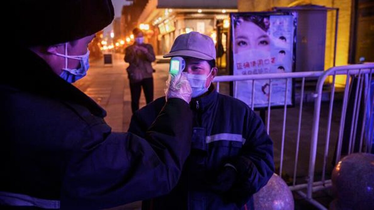 Un homme portant un masque de protection fait subir à une dame un contrôle de température