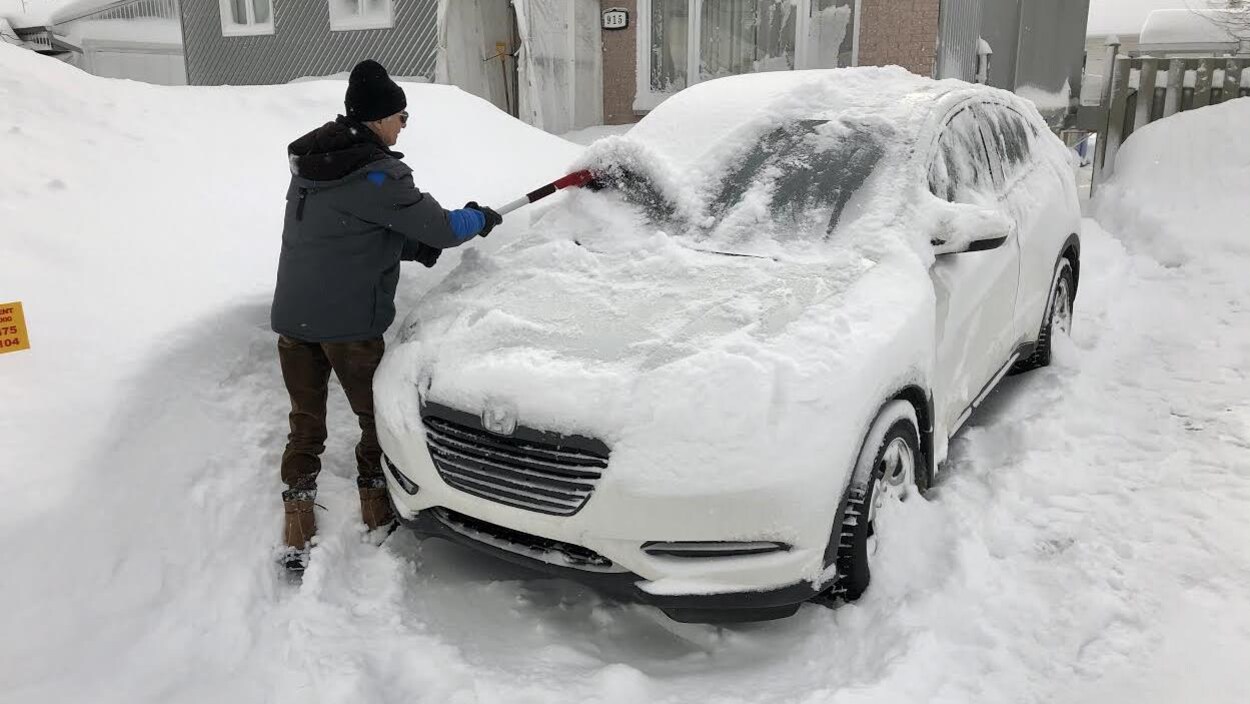 Un homme déneige sa voiture au lendemain de la tempête.