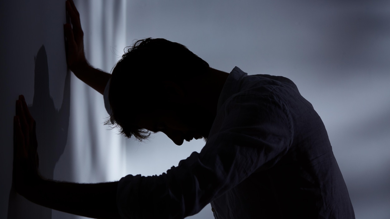Un homme dans l'ombre s'appuie au mur.