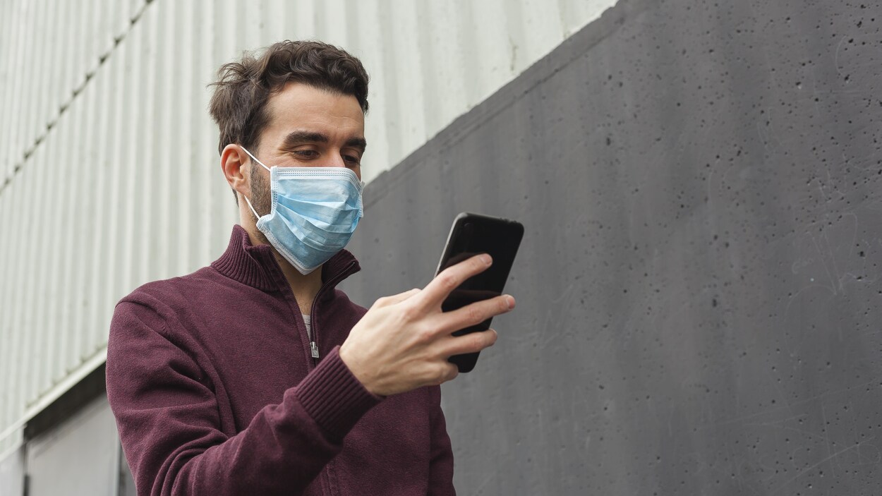 Un homme portant un masque chirurgical marche en regardant son téléphone intelligent.