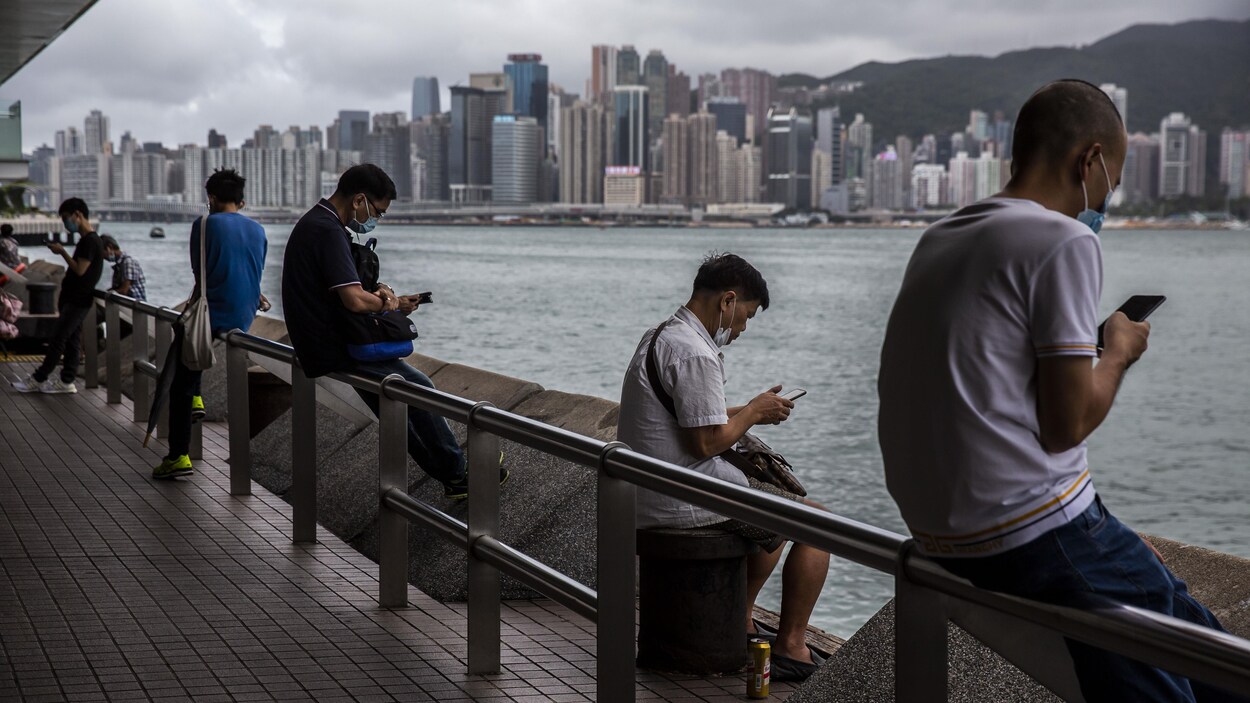 Des Hongkongais consultent leur téléphone intelligent assis sur la promenade Tsim Sha Tsui, à côté du port Victoria de Hong Kong.