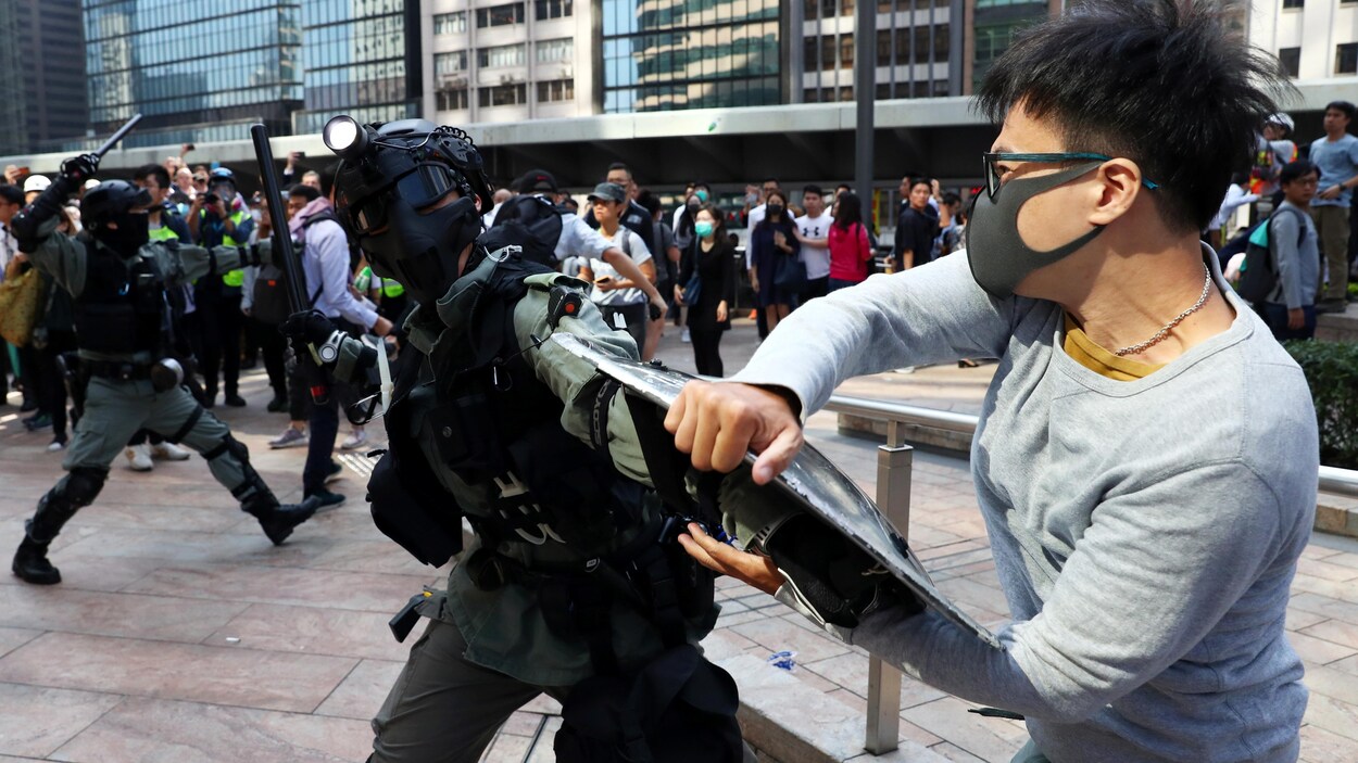 Un manifestant agrippe le bouclier d'un policier antiémeute, qui brandit une matraque.