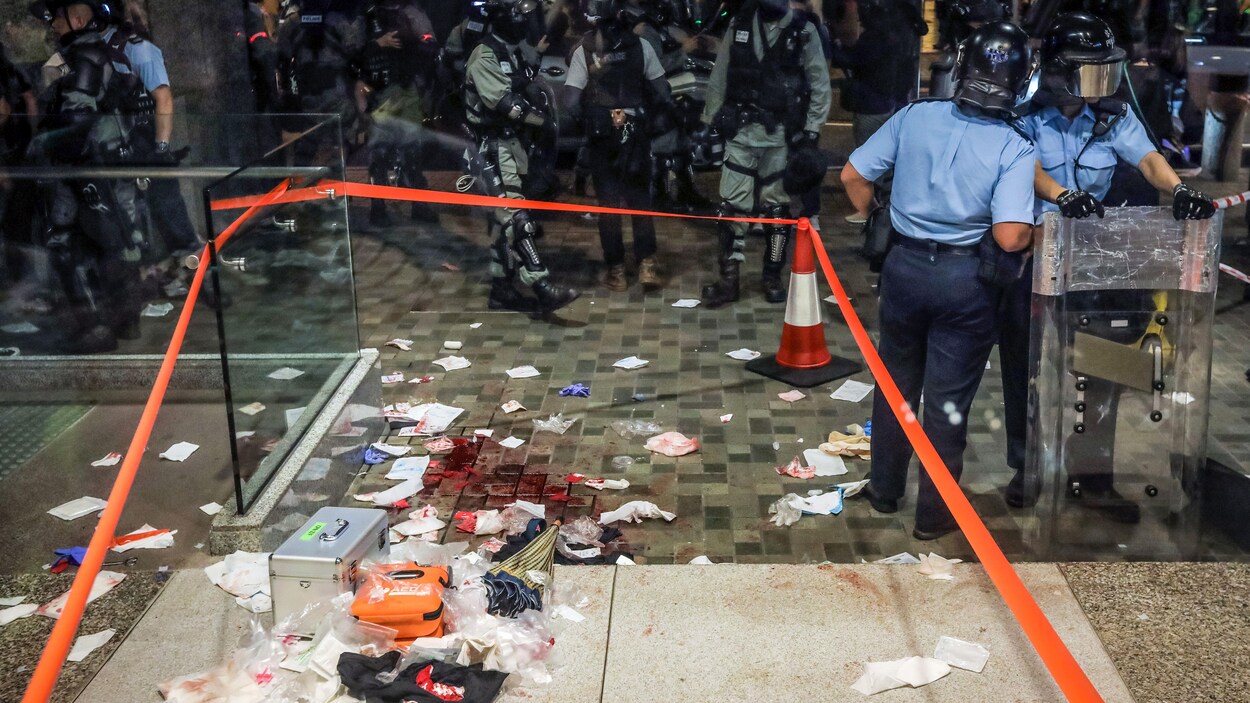 Du sang et des débris sont visibles sur le sol d'un centre commercial; la scène est entourée de policiers en tenue d'assaut.