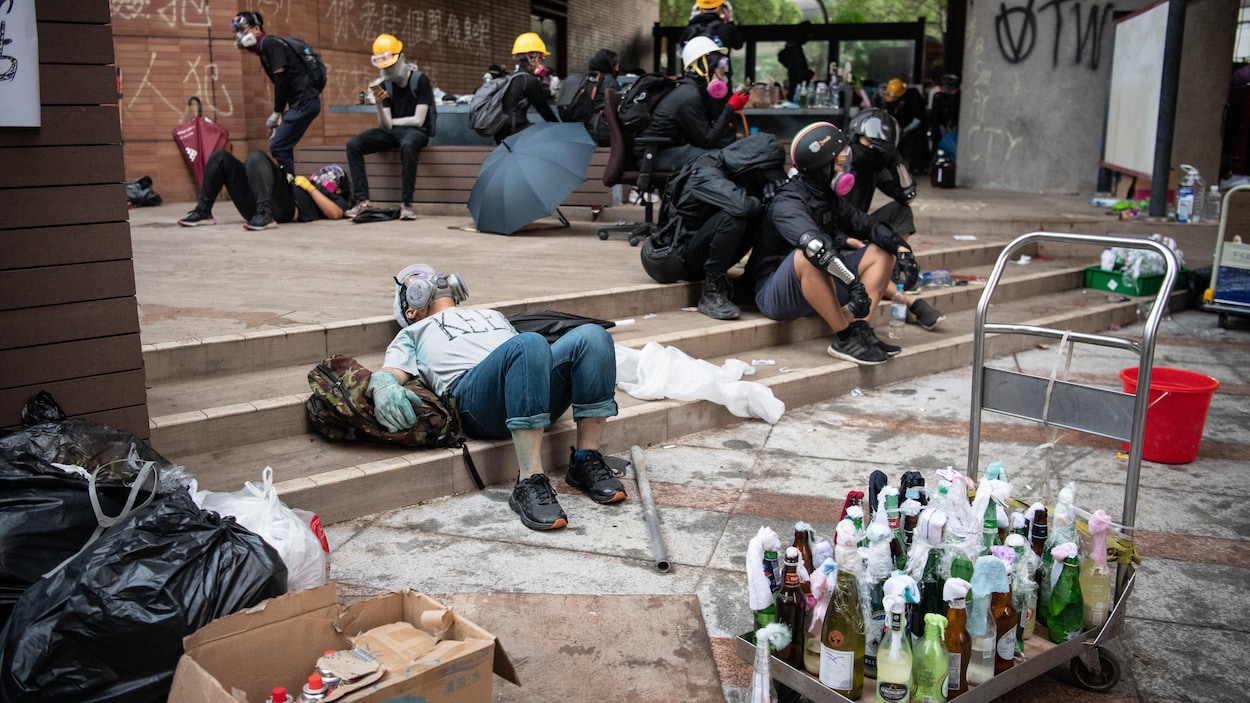 Des manifestants casqués et portant des masques à gaz sont couchés ou assis près d'un chariot contenant des dizaines de cocktails Molotov.