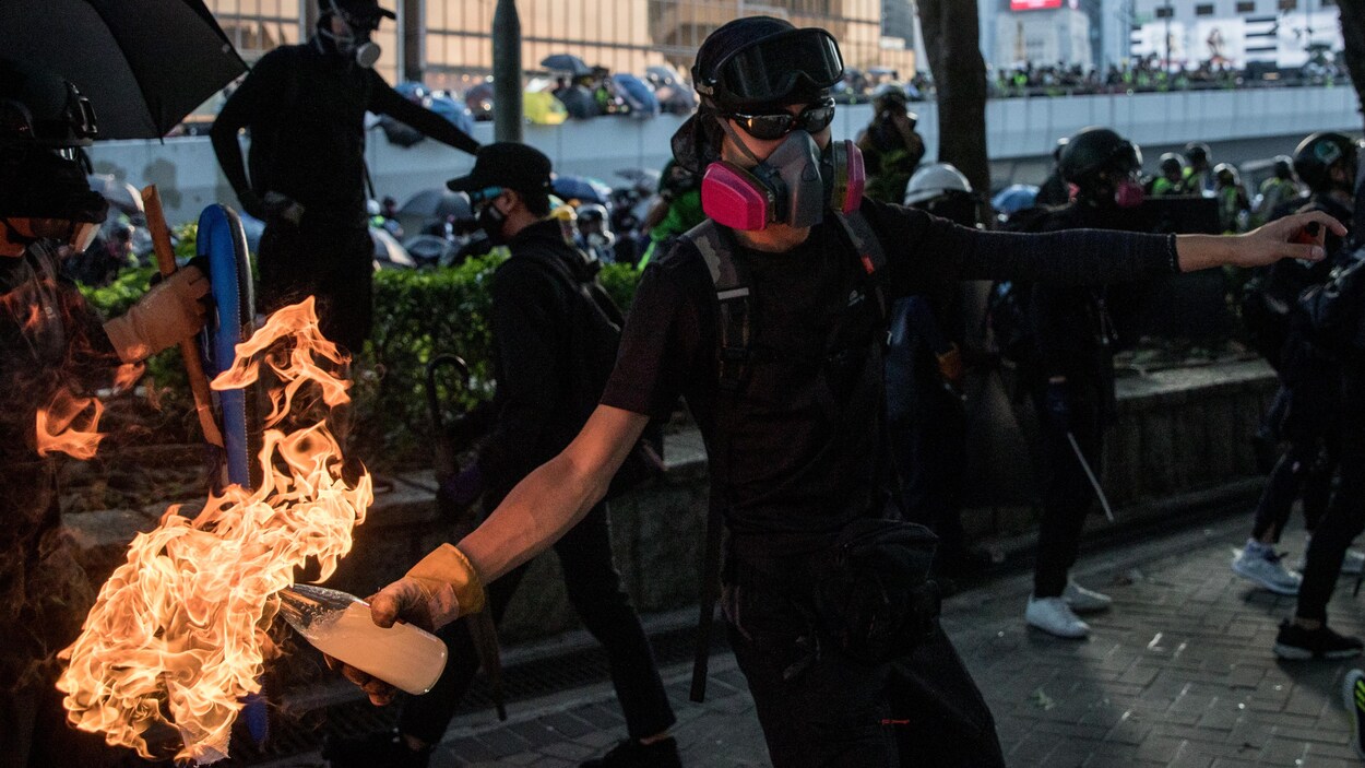 Un homme masqué tient une bouteille de plastique en feu.