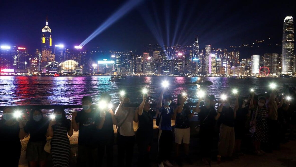 Des gens tiennent leur téléphone devant la ligne d'horizon de Hong Kong.