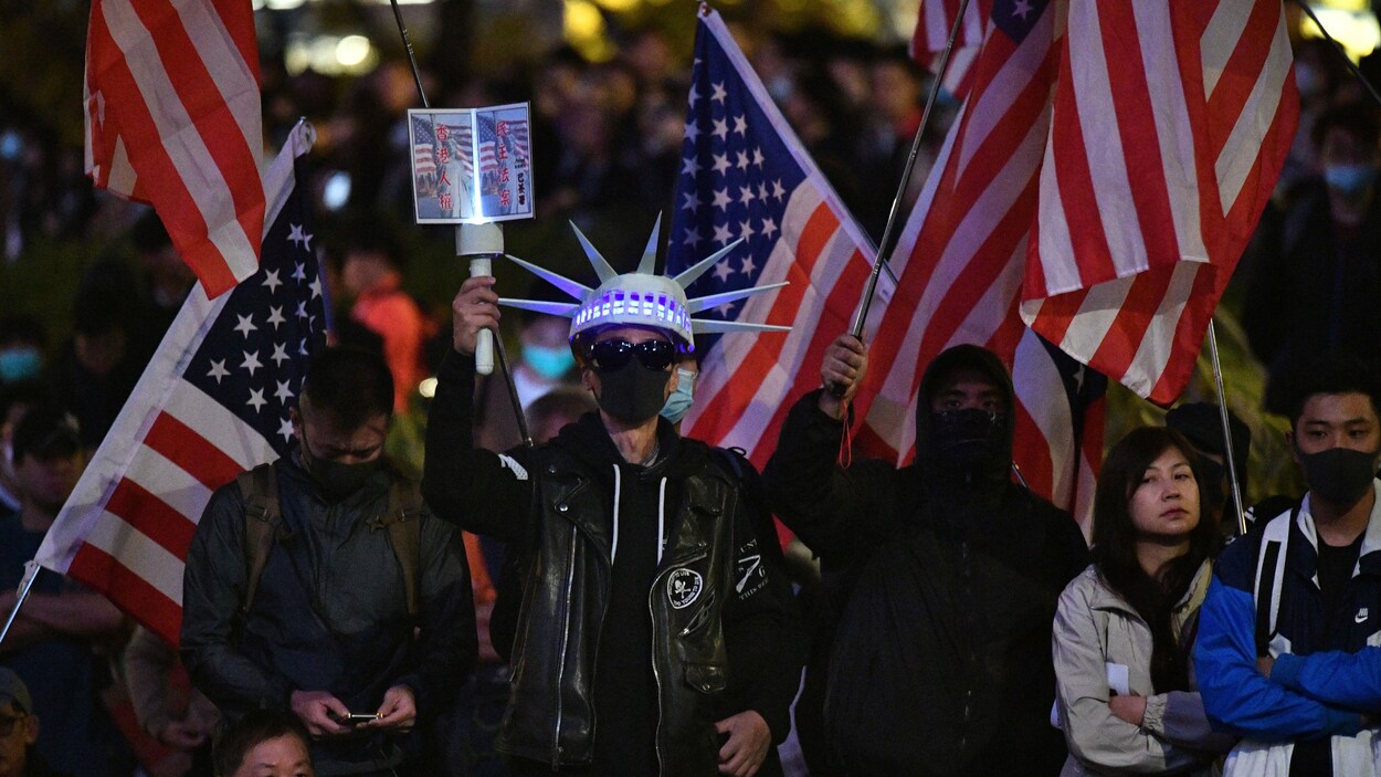 Trois hommes masqués brandissent des drapeaux américains au milieu d'une foule. L'un d'eux est déguisé en statue de la liberté.