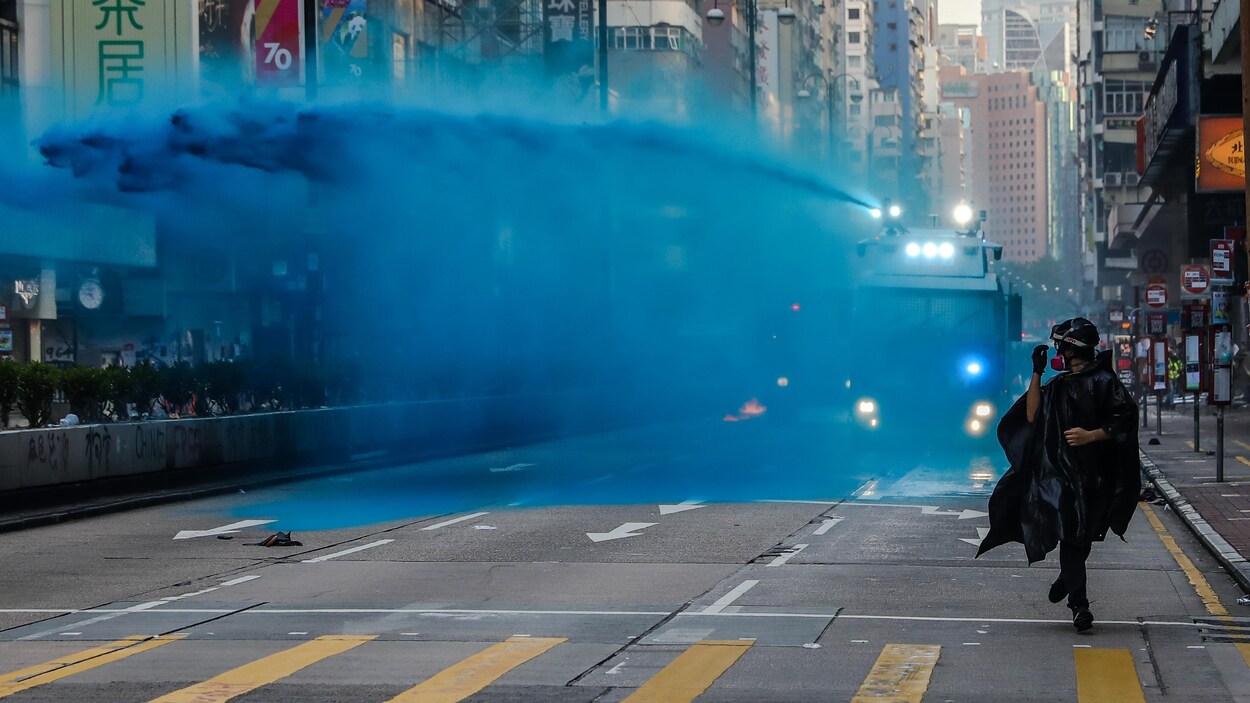 Dans une rue de Hong Kong, un manifestant court, poursuivi par un camion qui projette un liquide bleu, le 20 octobre 2019.